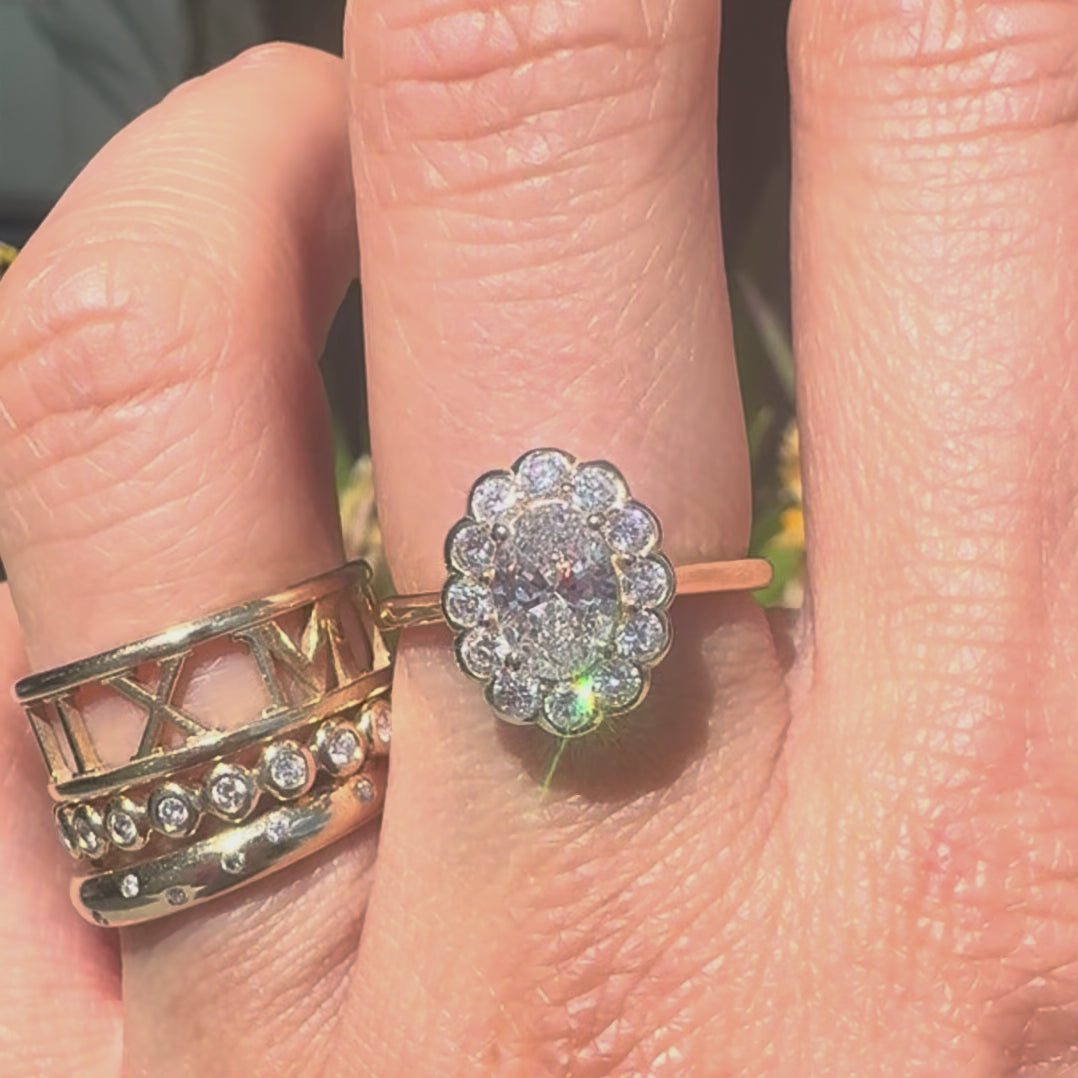 Oval diamond ring worns on a hand along with gold bands against a store window