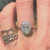 Oval diamond ring worns on a hand along with gold bands against a store window