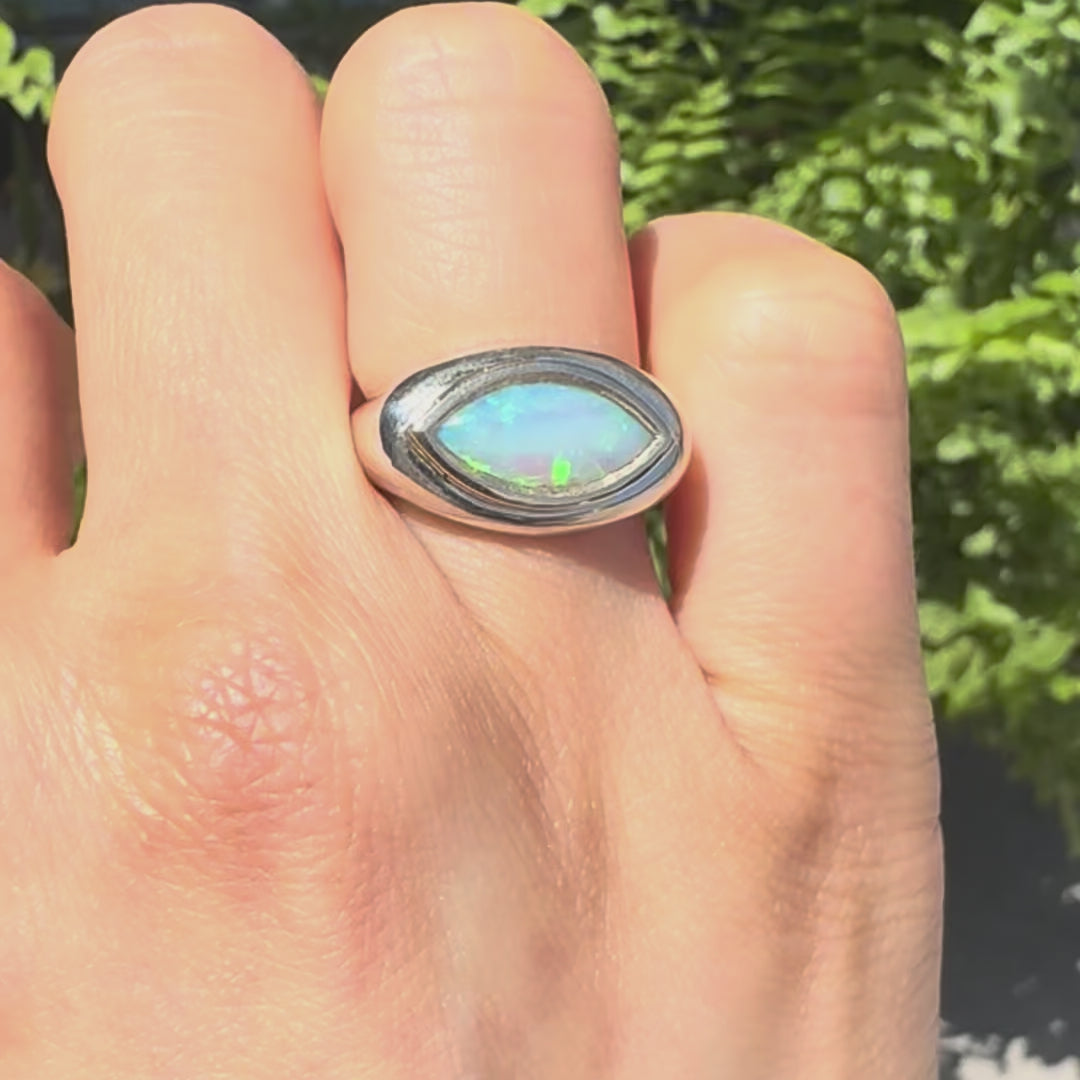 opal stone marquise shaped ring on a hand against a green background
