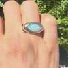 opal stone marquise shaped ring on a hand against a green background