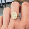 Oval ring with a hexagon shaped diamond in the center worn on a hand  against a gray background. 