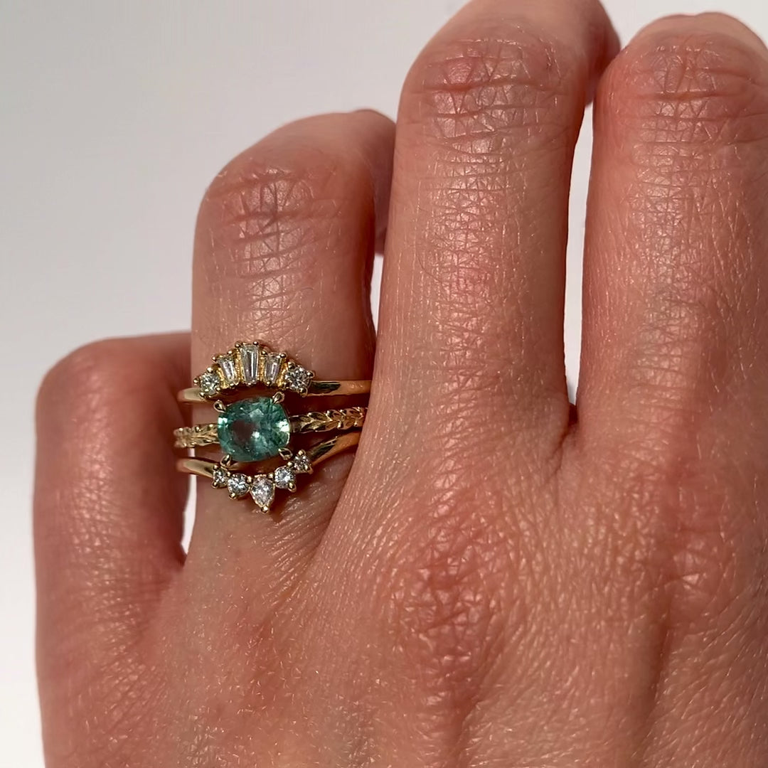 Jamie Park Jewelry -Meadow 1.16ct Cushion Montana Sapphire Ring Indulge in the beauty of nature with our Meadow Montana Sapphire Ring. Featuring a 1.16ct cushion cut sapphire, east-west set on an olive leaf band, this piece is perfect for an engagement ring or a special gift. The Montana sapphire's blue and green hues make it a truly one-of-a-kind piece to celebrate life's special moments.