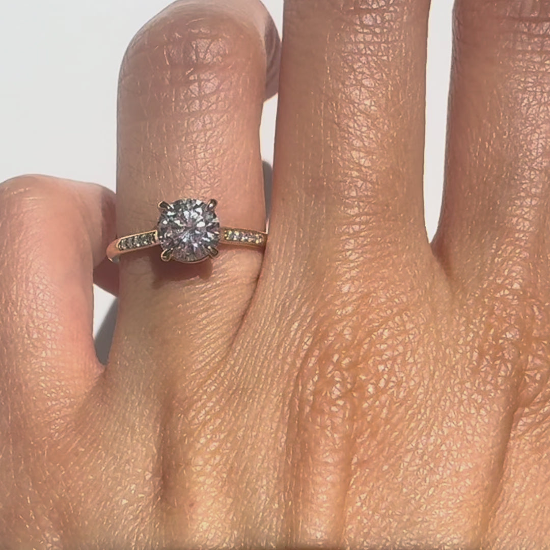 Round diamond rings on a finger against a neutral background
