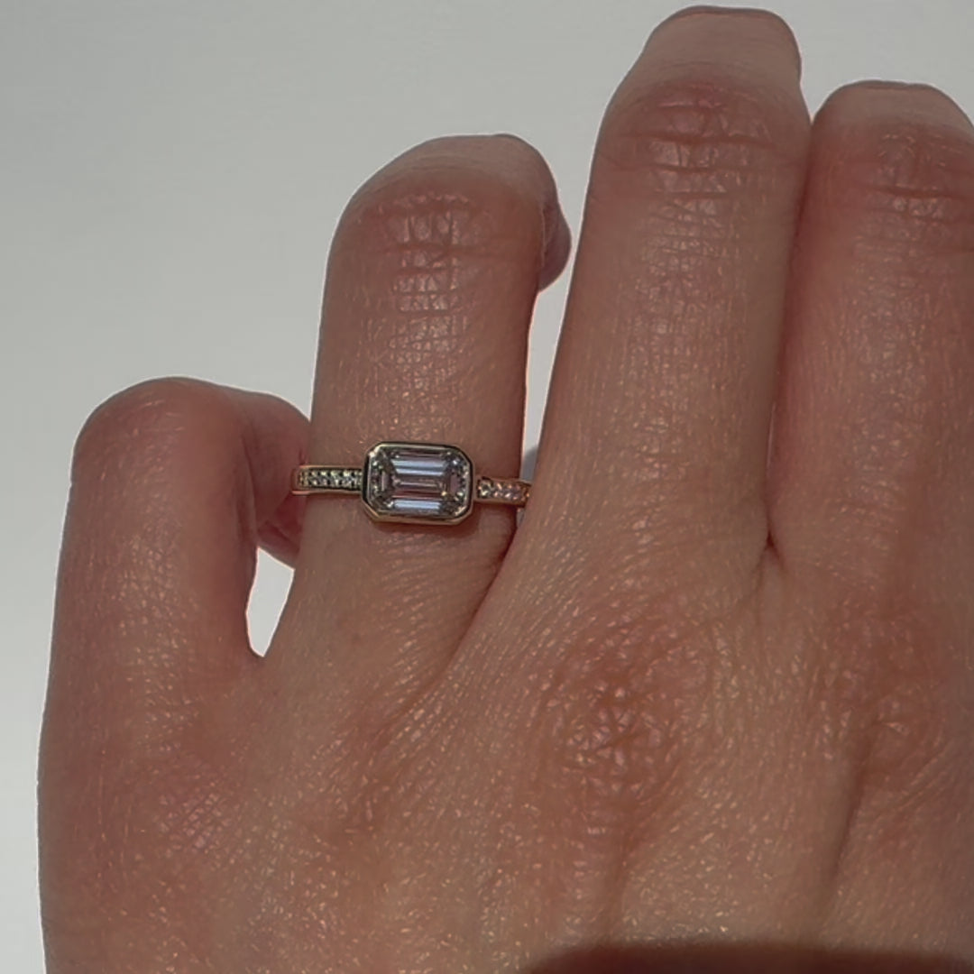The Zoey Ring features a 1-carat emerald-cut diamond or moissanite in an east-west setting. The smooth bezel setting ensures everyday wear, while delicate accent diamonds add sparkle from every angle