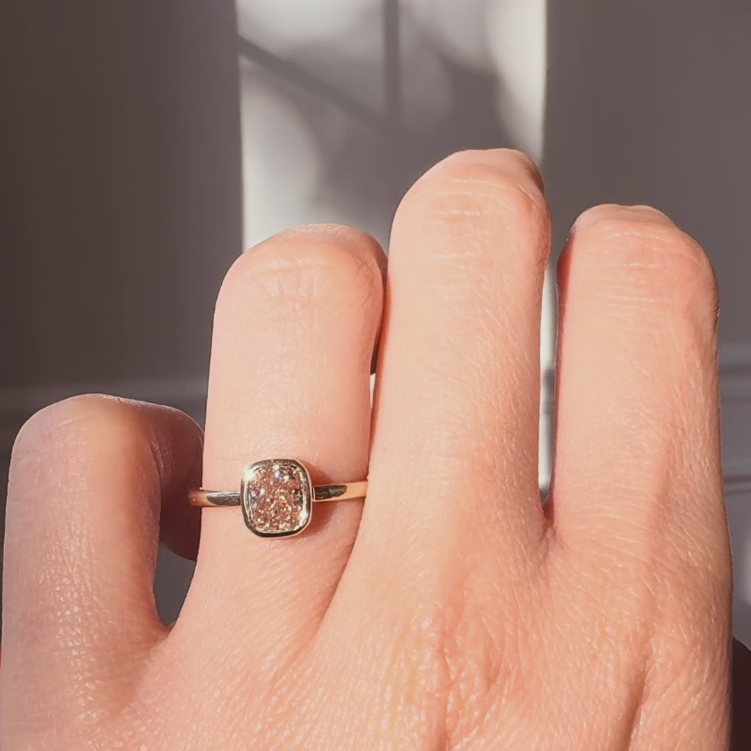 Champagne color diamond ring worn on a hand against a neutral background