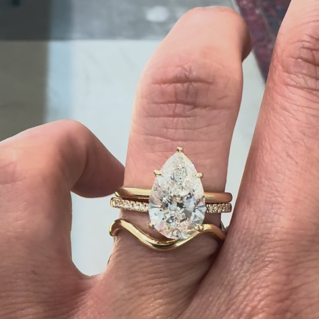 A pear cut diamond ring and wedding bands a on a hand against gray background.