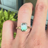A close-up of a hand wearing a gold ring with a rectangular emerald-cut green gemstone.