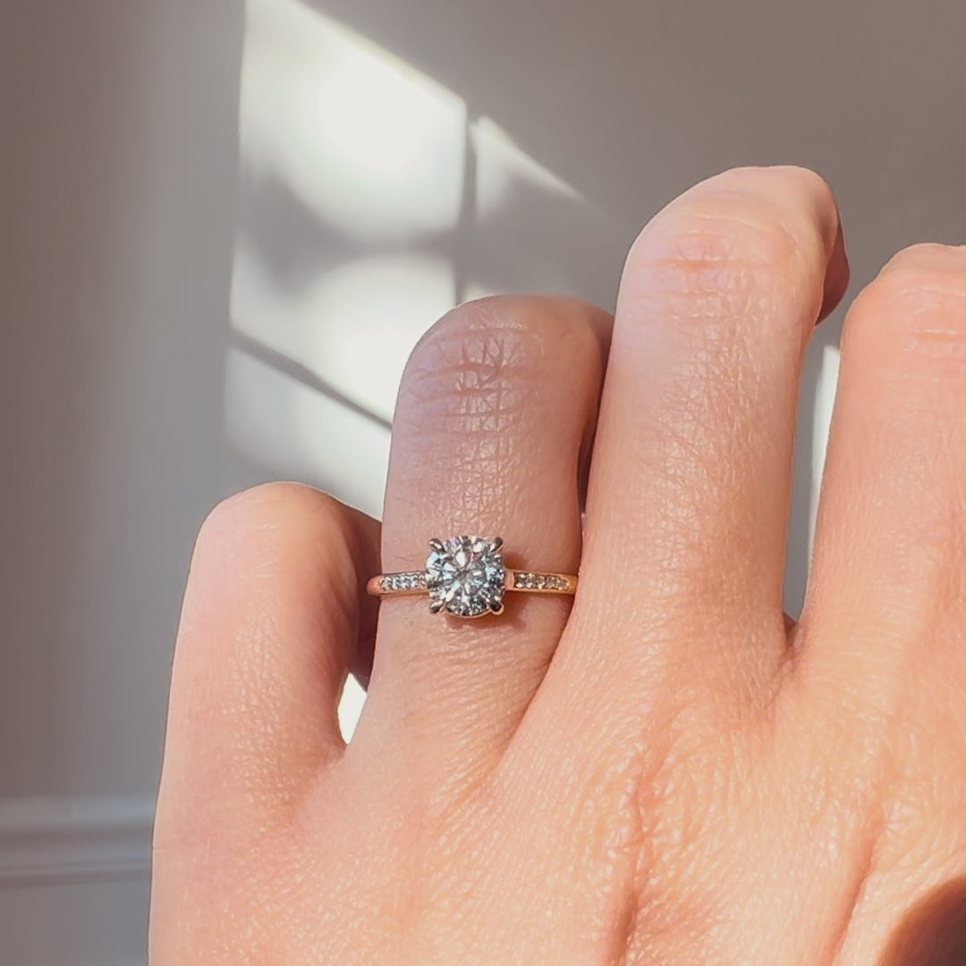 Round diamond ring on a hand against a neutral background. 