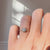 Round diamond ring on a hand against a neutral background. 