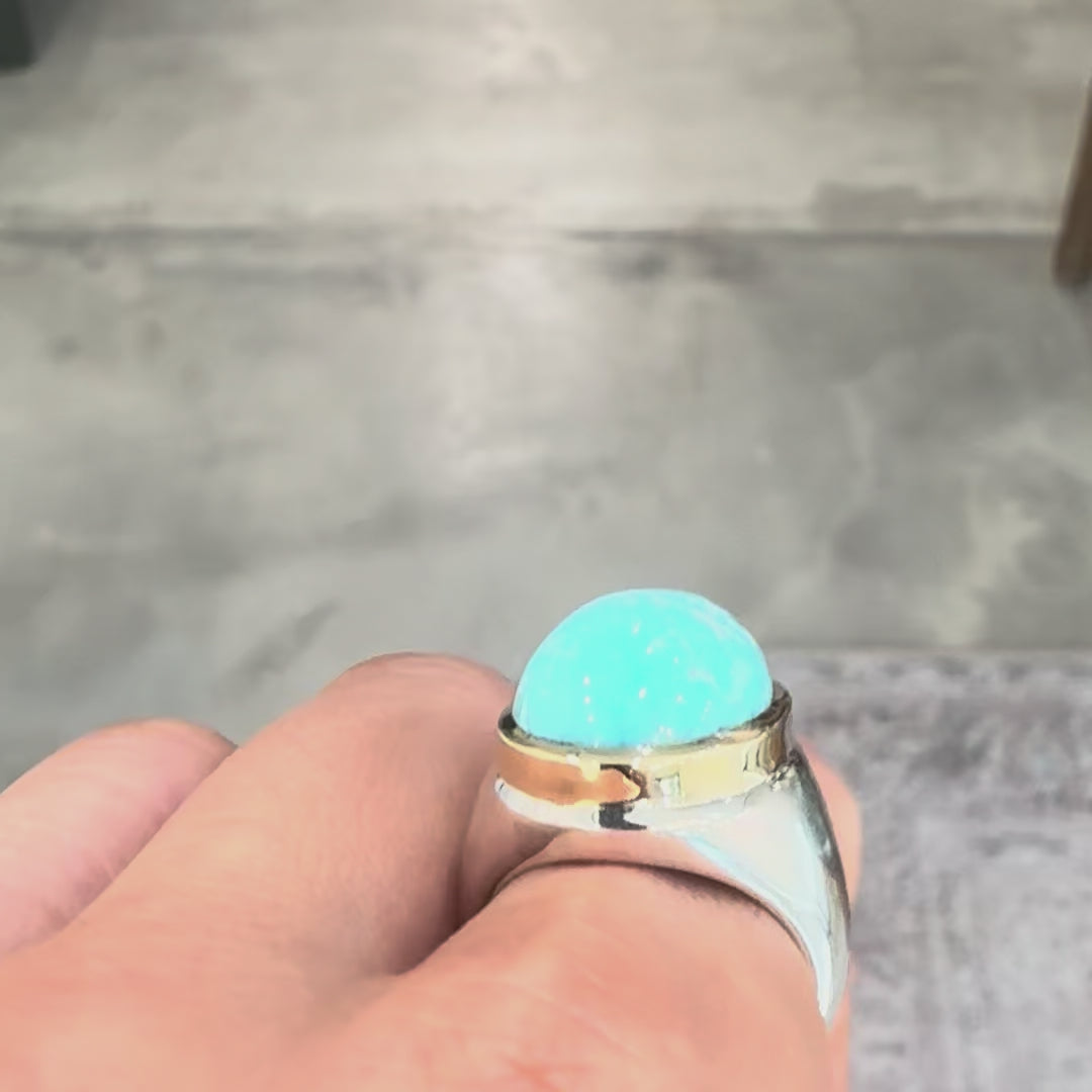 oval turquoise set on a gold and silver combo ring worn on a hand against a gray backgroun. 