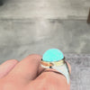 oval turquoise set on a gold and silver combo ring worn on a hand against a gray backgroun. 
