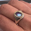 Ring with a blue moonstone and gold bezel setting on a silver band on a hand in an indoor background. 