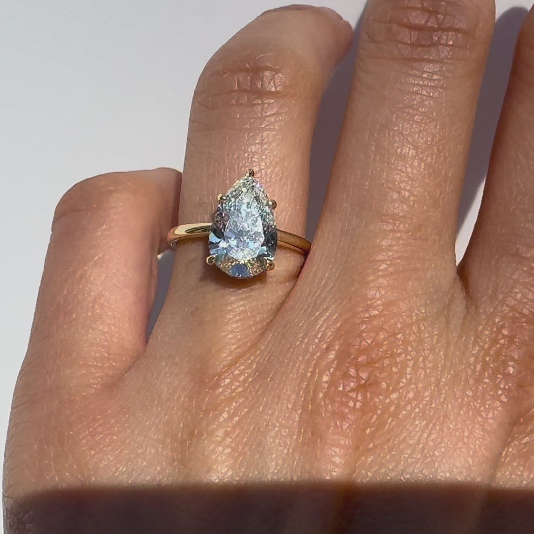 A pear cut diamond ring on a hand against white background.