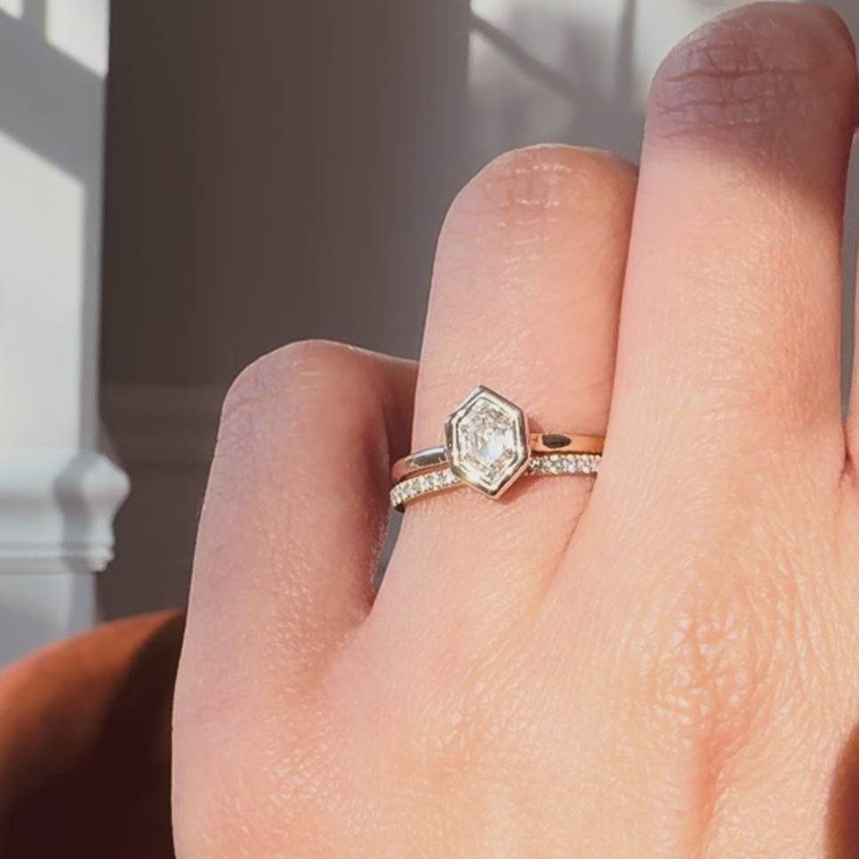 hexagon diamond ring and a diamond band worn on  a hand against neutral background. 