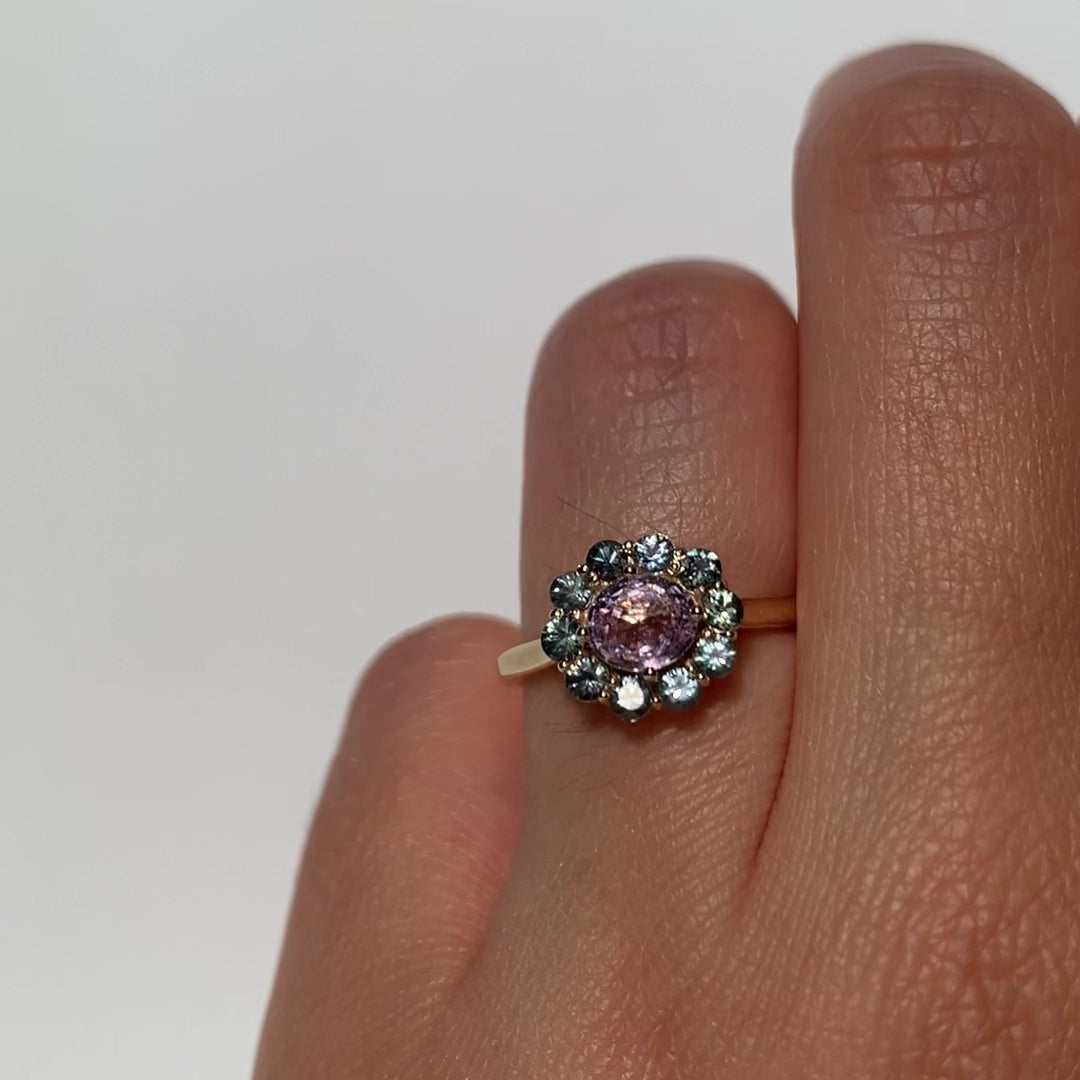 The 1.4 ctw. Pink Sapphire Charlotte Ring features a 3/4ct light pink sapphire at the center, framed by a variety of toned teal sapphires. The sweet and colorful halo design is truly one of a kind. This ring is perfect for those who appreciate timeless and unique designs. The slightly raised setting makes this ring fully stackable.