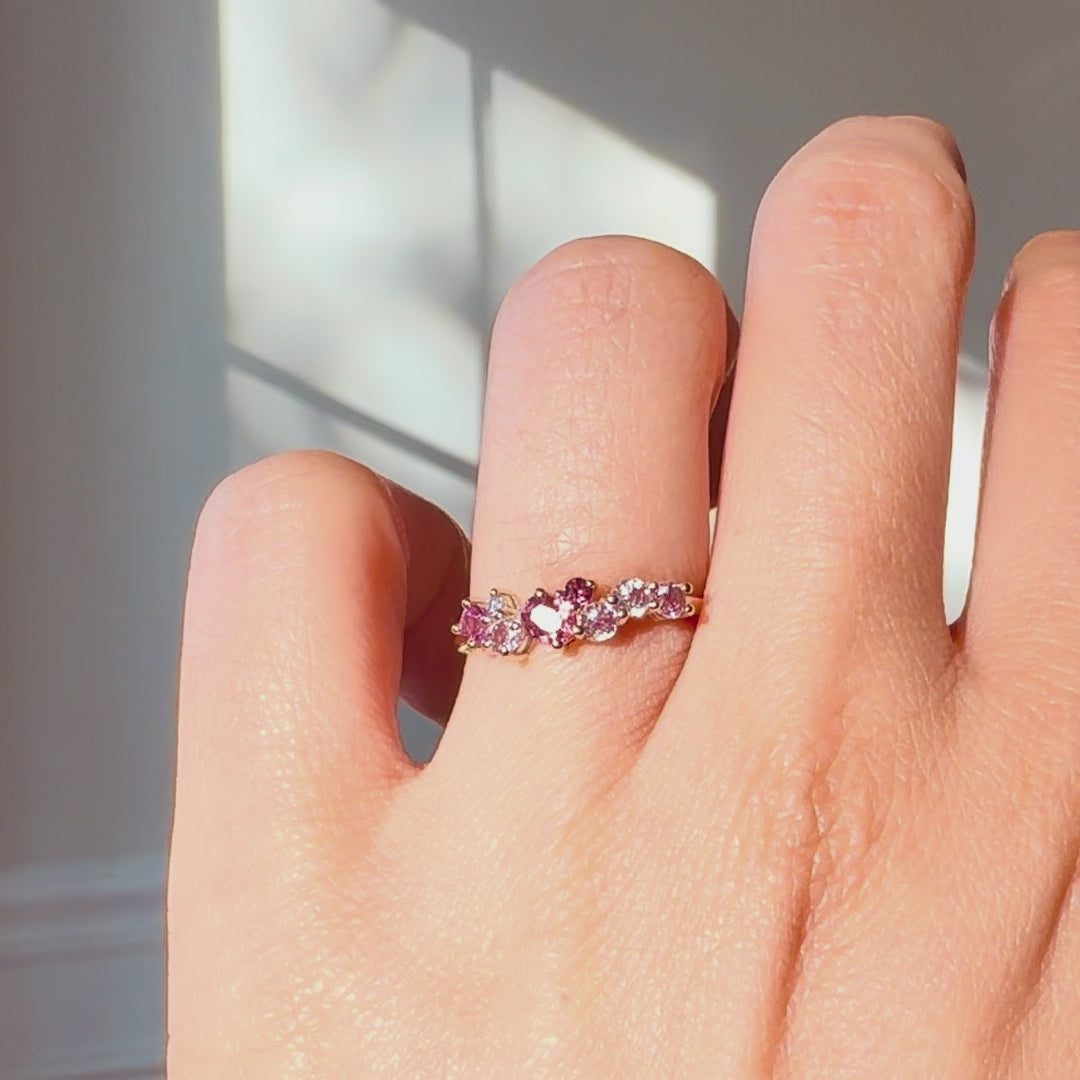pink sapphire ring worn on  a hand against neutral background. 