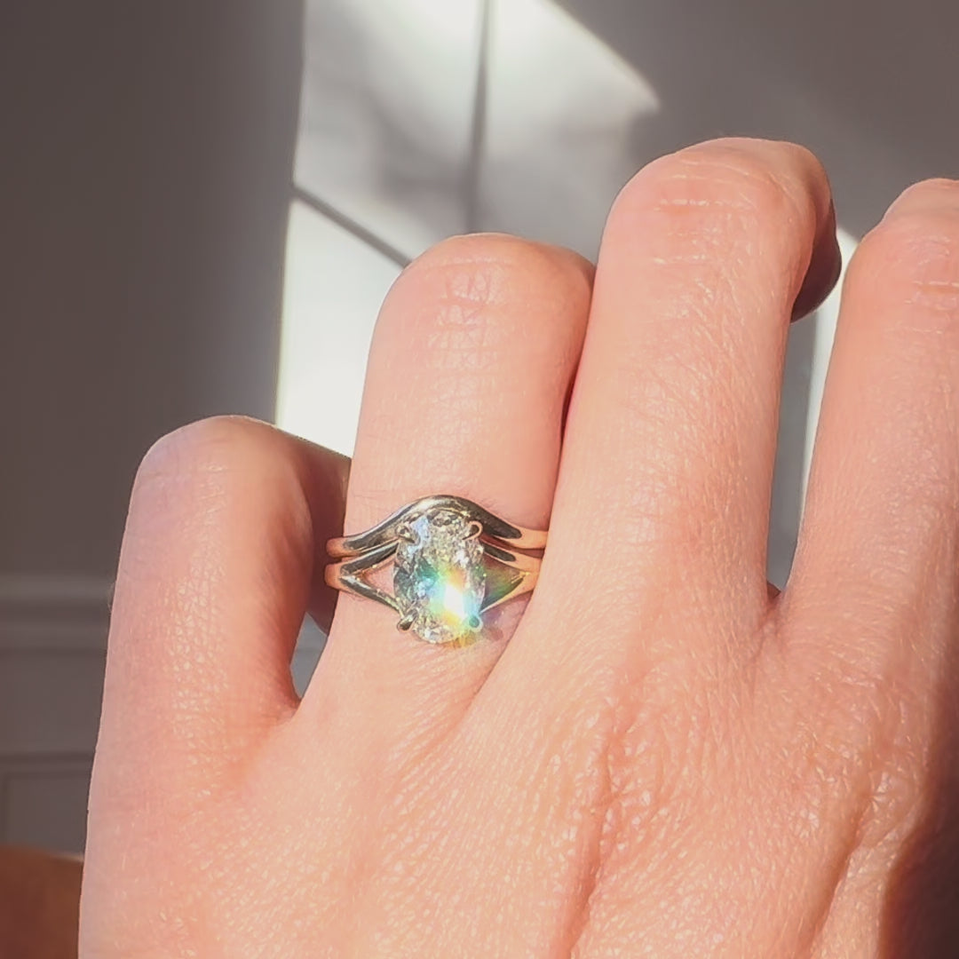 oval diamond engagement ring and a wedding band on a hand against a neutral background